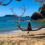 Woman sitting on a low hanging branch over a sandy beach in Costa Rica