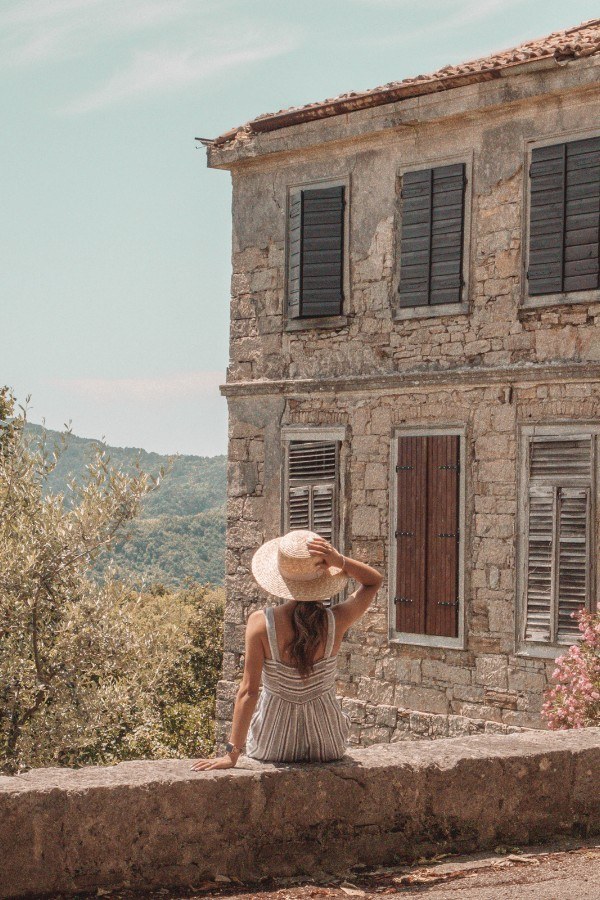 A woman in a straw hat sitting on a stone wall.